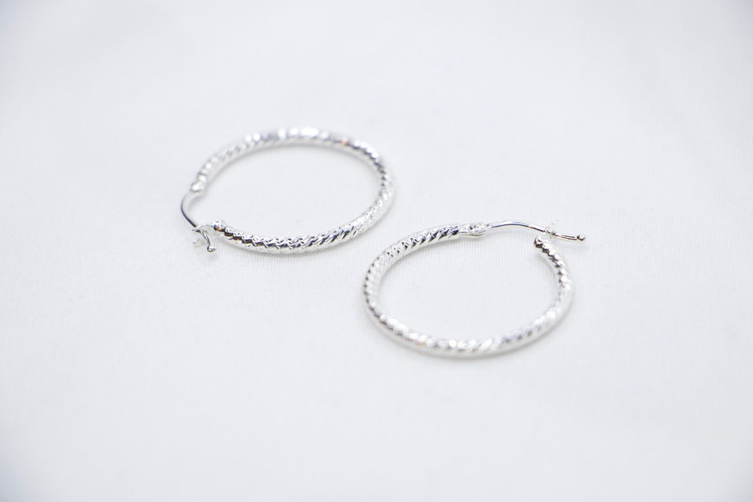 A close-up of sterling silver Woven Elegance Hoop Earrings featuring an intricate woven texture side views.
