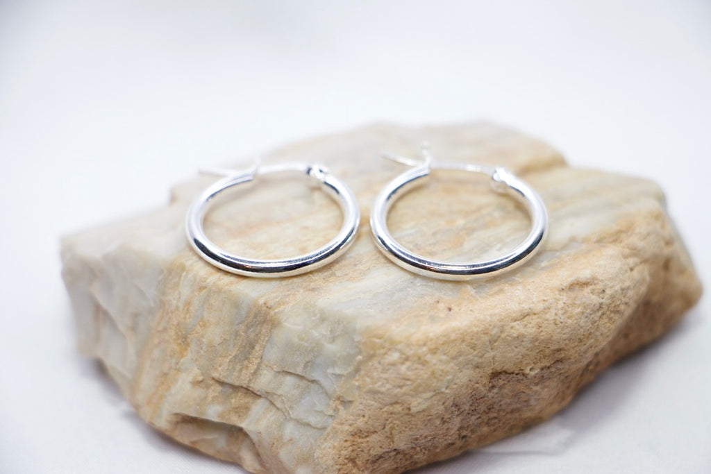 Sterling silver Eternal Grace Hoop Earrings featuring a smooth, polished circular design with an X-shaped closure for a unique, elegant look, rock view.