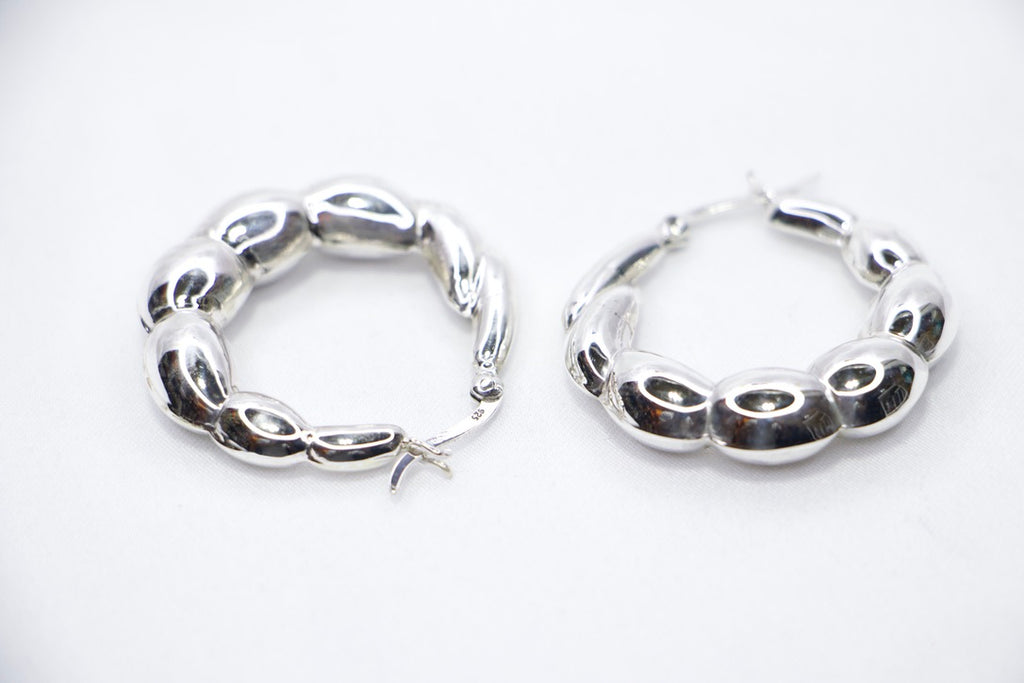 A close-up of sterling silver Luxe Bean Hoop Earrings, designed with smooth, curved shapes that form a modern, elegant hoop side view.
