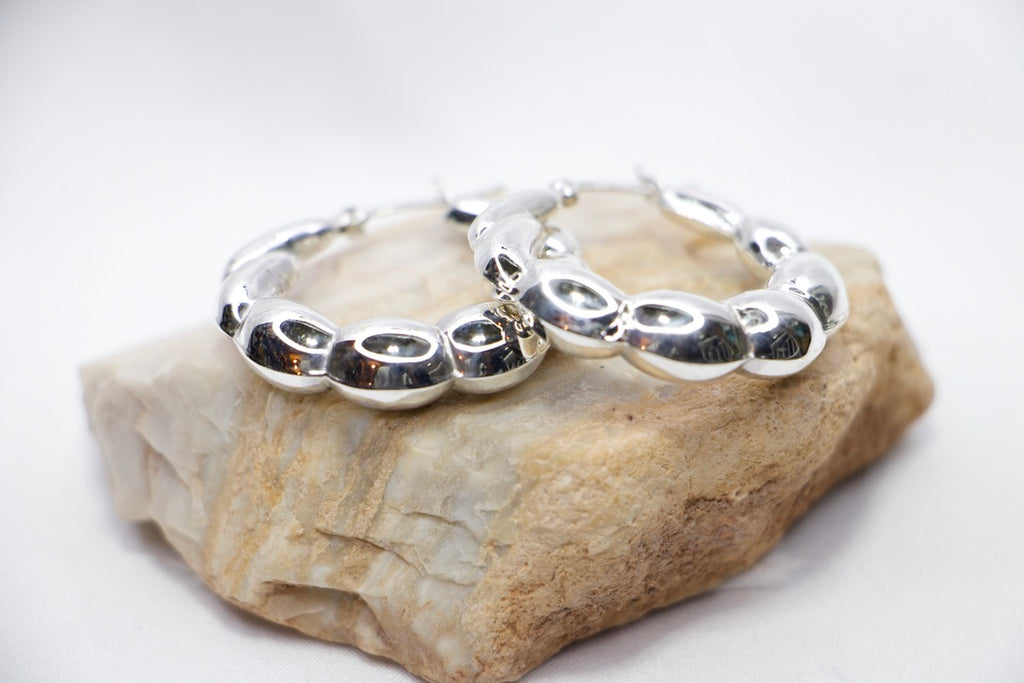 A close-up of sterling silver Luxe Bean Hoop Earrings, designed with smooth, curved shapes that form a modern, elegant hoop rocks view.