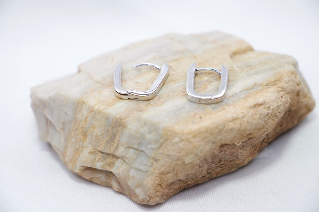 A pair of Sleek Seduction Huggie Hoops in 925 sterling silver, featuring a modern rectangular design with a high-polish finish, rock view.
