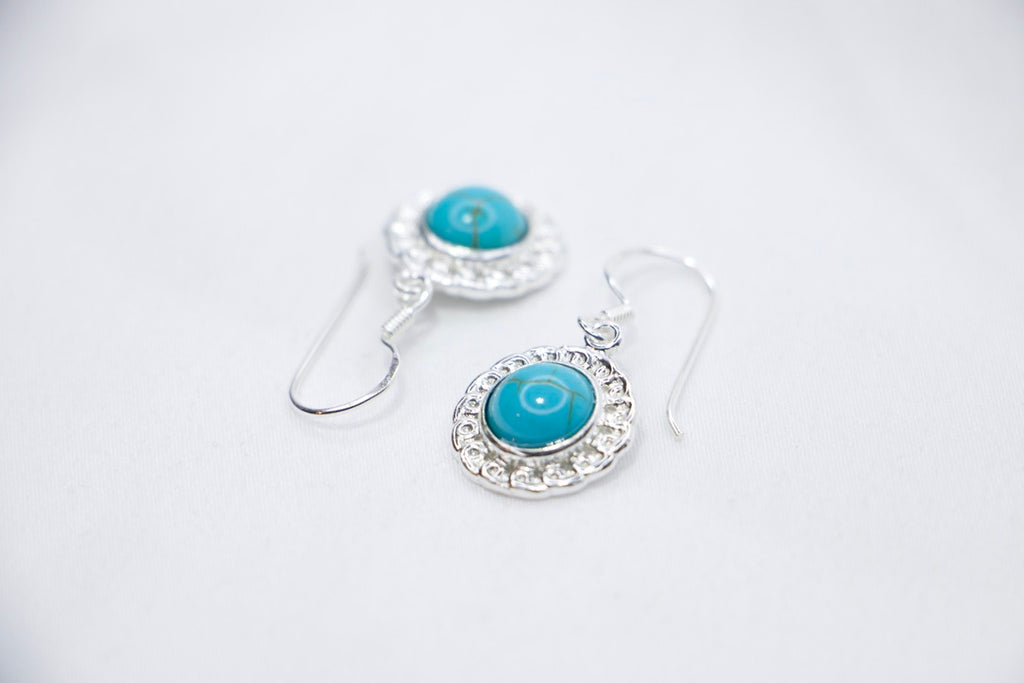 A Turquoise Serenity Drop Earrings featuring a vibrant turquoise gemstone set in a delicate sterling silver frame with an ornate design, sides views.