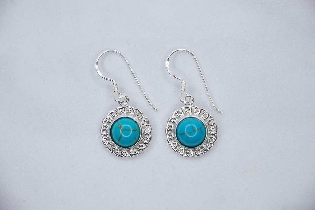 A Turquoise Serenity Drop Earrings featuring a vibrant turquoise gemstone set in a delicate sterling silver frame with an ornate design, top views.