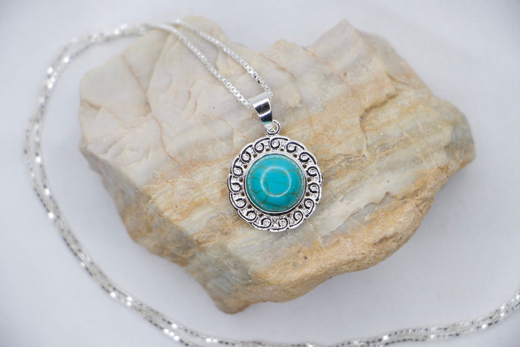 A Turquoise Serenity Drop Earrings featuring a vibrant turquoise gemstone set in a delicate sterling silver frame with an ornate design, rock view.