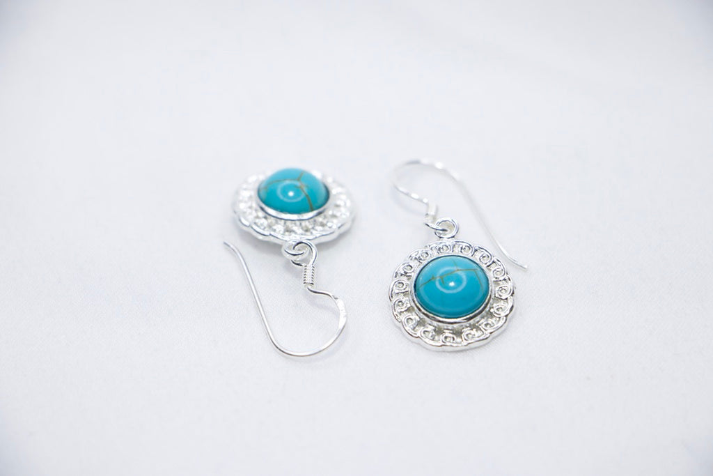 A Turquoise Serenity Drop Earrings featuring a vibrant turquoise gemstone set in a delicate sterling silver frame with an ornate design, side views.
