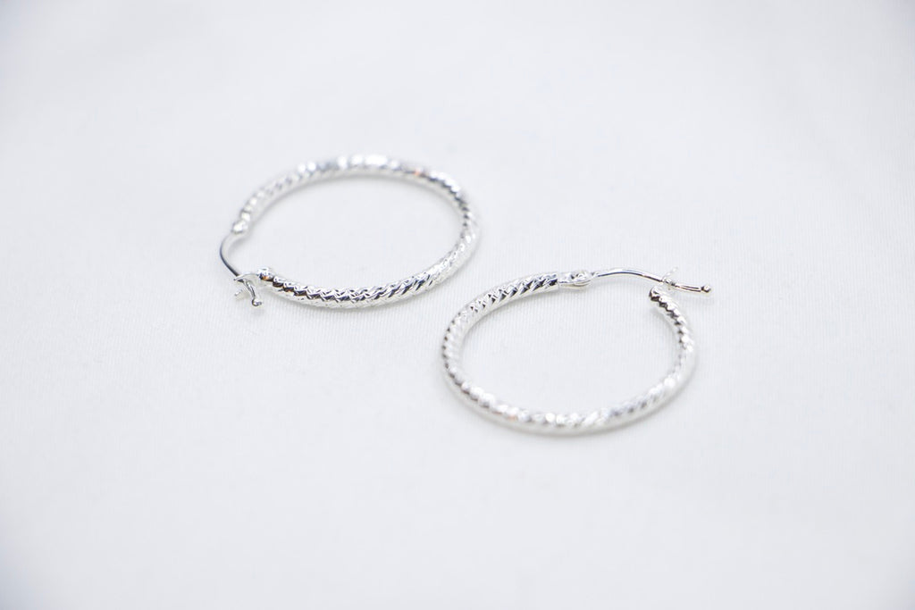 A close-up of sterling silver Woven Elegance Hoop Earrings featuring an intricate woven texture side views.