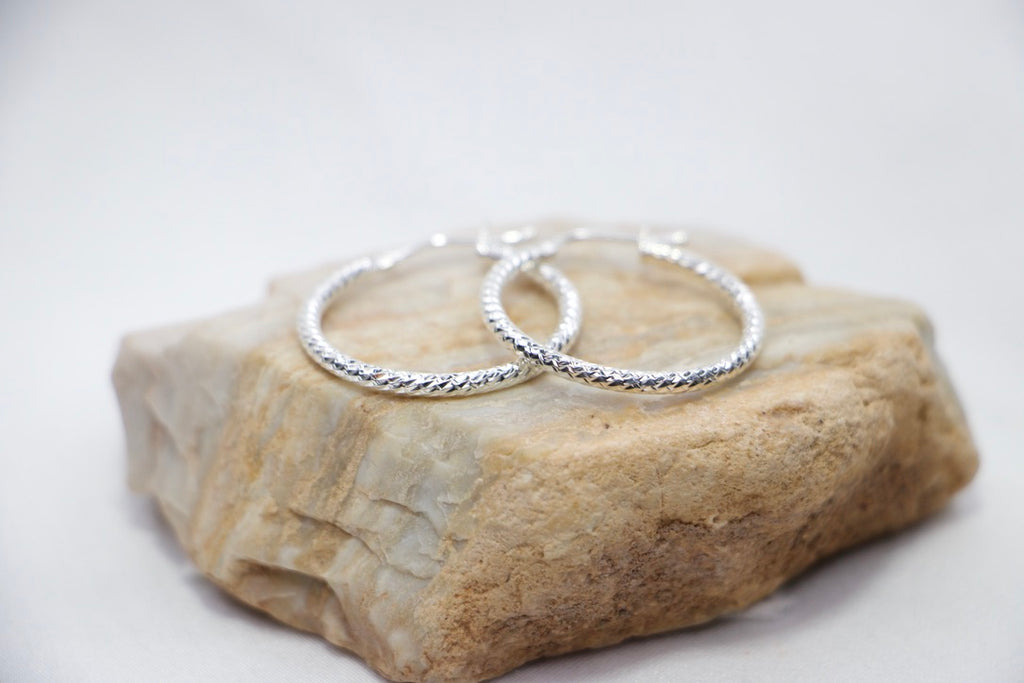 A close-up of sterling silver Woven Elegance Hoop Earrings featuring an intricate woven texture rock view.
